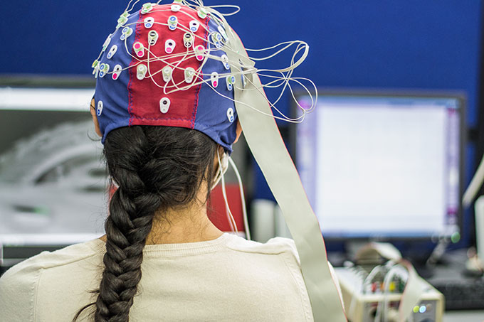 a woman sitting in front of the viewer wears an EEG cap